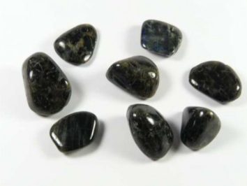 Osiem ciemnych, wygładzonych kamieni leży na białym tle.