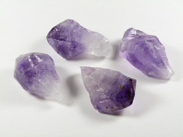 Cztery surowe kryształy ametystu na białym tle.