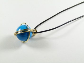 Naszyjnik z niebieską kulką oplecioną złotym drutem na czarnym sznurku.