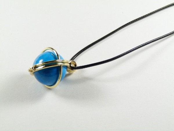 Naszyjnik z niebieską kulką oplecioną złotym drutem na czarnym sznurku.