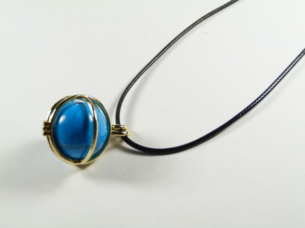 Naszyjnik z niebieskim kamieniem w złotej oprawie na czarnym sznurku.