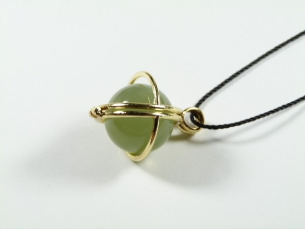 Wisiorek z zieloną kulką otoczoną złotymi obręczami na czarnym sznurku, na białym tle.