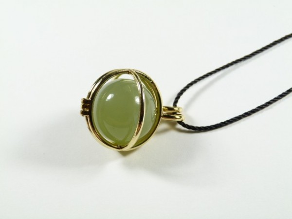 Złoty wisiorek z zielonym kamieniem na czarnym sznurku, leży na białym tle.