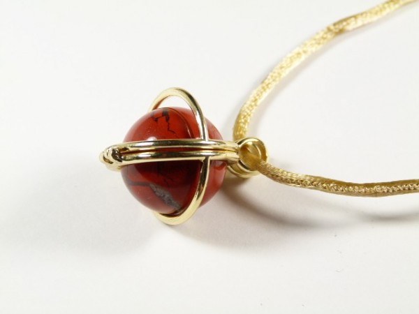 Złoty naszyjnik z czerwoną kulką ozdobną w złotej oprawie na białym tle.