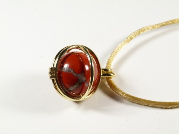 Złoty wisior z czerwonym kamieniem na jasnym sznurku, ujęcie z góry.