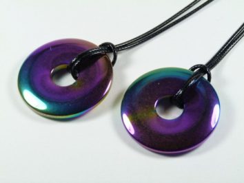 Dwa tęczowe wisiorki w kształcie pierścieni na czarnych sznurkach.