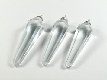 Trzy przezroczyste kryształowe zawieszki leżące na białym tle.