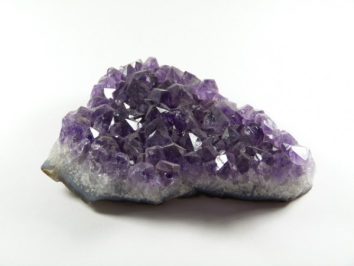 Fioletowa geoda ametystu leżąca na białym tle.