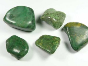Pięć zielonych, wygładzonych kamieni leży na białym tle.