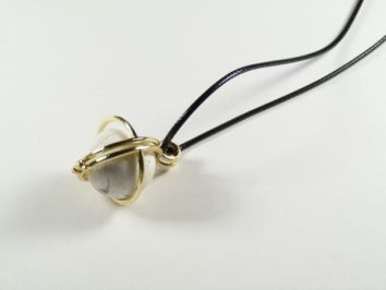 Wisiorek z kamieniem oprawionym w złoty drut na czarnym skórzanym rzemyku.