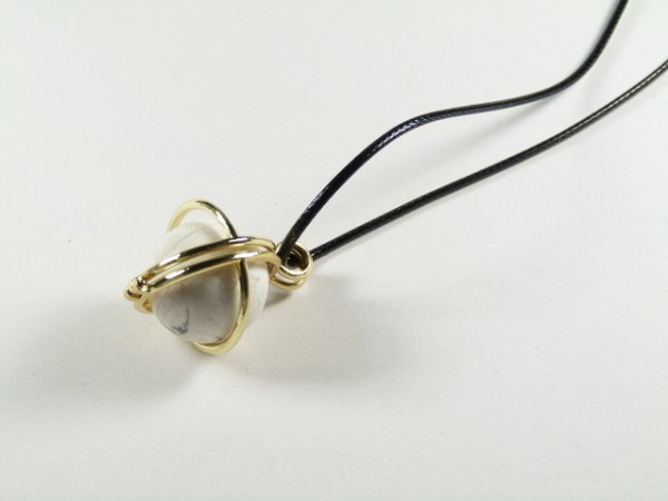 Wisiorek z kamieniem oprawionym w złoty drut na czarnym skórzanym rzemyku.