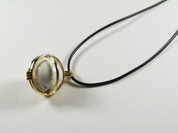 Wisiorek z przezroczystym kamieniem w złotej oprawie na czarnym sznurku.