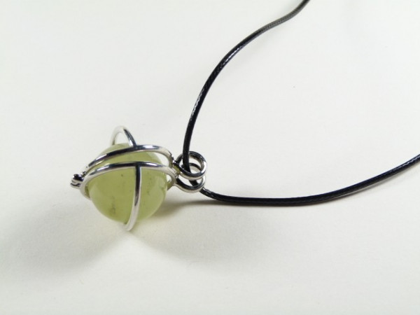 Naszyjnik z zielonym kamieniem oprawionym w metal, na czarnym sznurku, na jasnym tle.