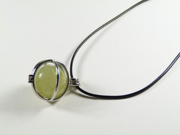 Wisiorek z zielonym kamieniem w srebrnej oprawie na czarnym sznurku.