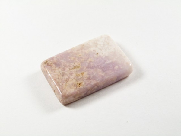 Prostokątny, polerowany kamień o jasnofioletowym kolorze leży na białym tle.