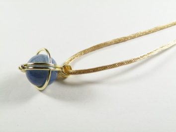 Złoty naszyjnik z niebieskim kamieniem oprawionym w metalową oprawę na białym tle.
