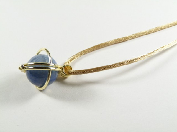 Złoty naszyjnik z niebieskim kamieniem oprawionym w metalową oprawę na białym tle.