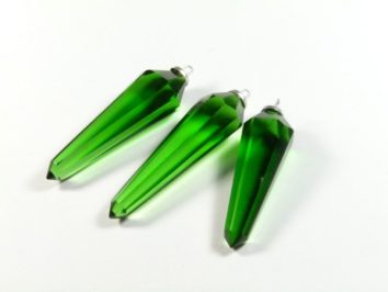 Trzy zielone, szklane ozdoby w kształcie sopli leżą na białym tle.