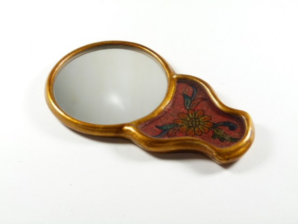 Małe lusterko z ozdobną ramką i kwiatowym wzorem na uchwycie, leżące na białym tle.