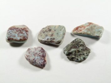 Pięć małych, płaskich kamieni o różnych kształtach i marmurkowych wzorach na białym tle.