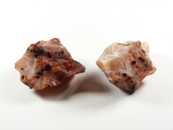 Dwa surowe, różowawe kamienie minerału leżące na białym tle.