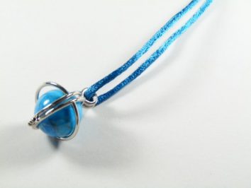 Niebieski naszyjnik z koralikiem owiniętym srebrnym drutem na jasnym tle.