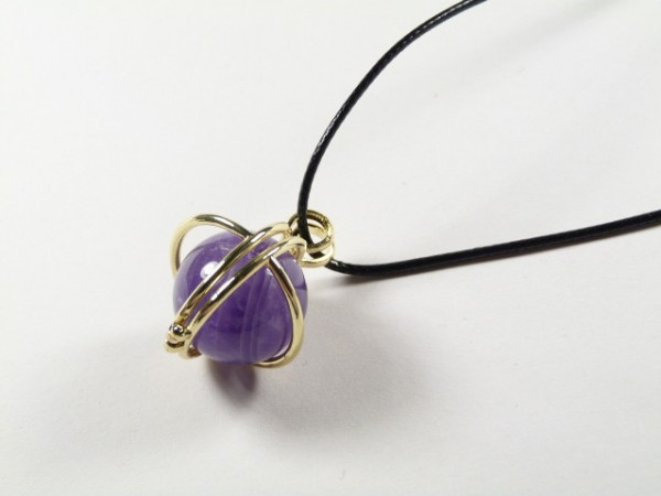 Naszyjnik z czarnym sznurkiem i fioletowym kamieniem w złotej oprawie.