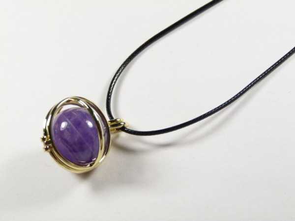 Naszyjnik z czarnym sznurkiem i fioletowym kamieniem oprawionym w złoty metal.