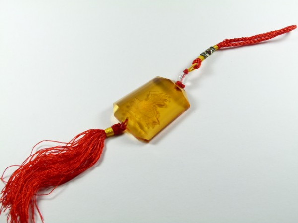Bursztynowy amulet z czerwonym frędzlem i sznurkiem leży na białym tle.