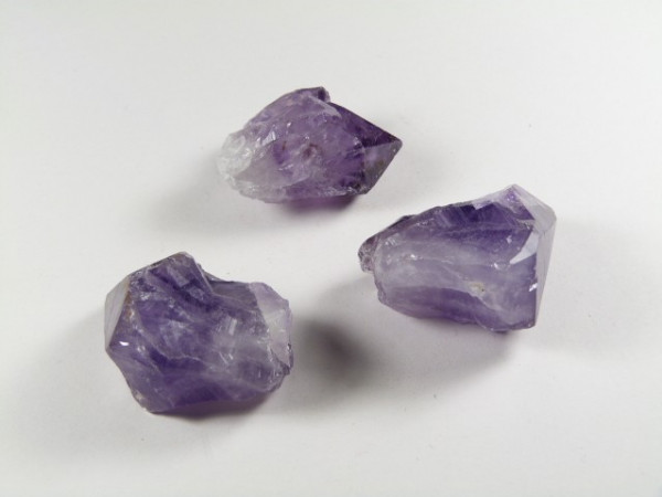 Trzy surowe kryształy ametystu leżące na białym tle.