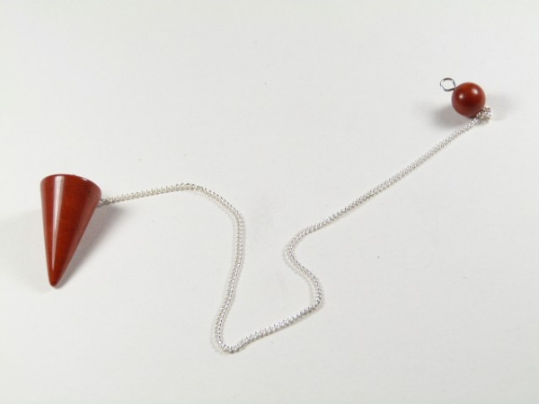 Wahadełko z czerwonego kamienia na srebrnym łańcuszku, leży na białym tle.