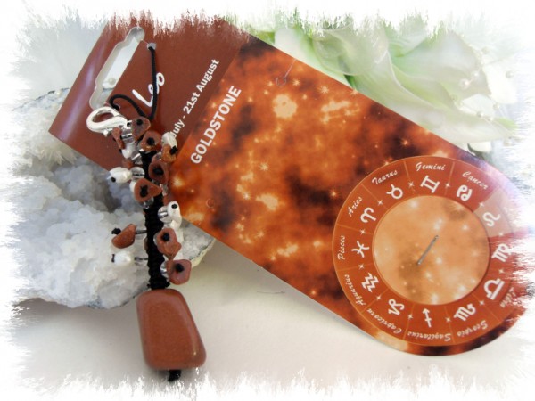 Breloczek z kamieniem goldstone na tle karty zodiaku Lwa i symbolami astrologicznymi.