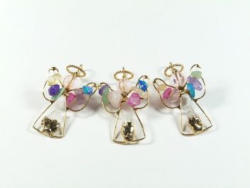 Trzy ozdoby w kształcie aniołków wykonane z drutu i kolorowych koralików na białym tle.