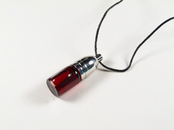 Olejek dragon's blood/ smocza krew - buteleczka wisiorek. Wisiorek w kształcie kapsułki z czerwonym płynem na czarnym sznurku, leży na białym tle.