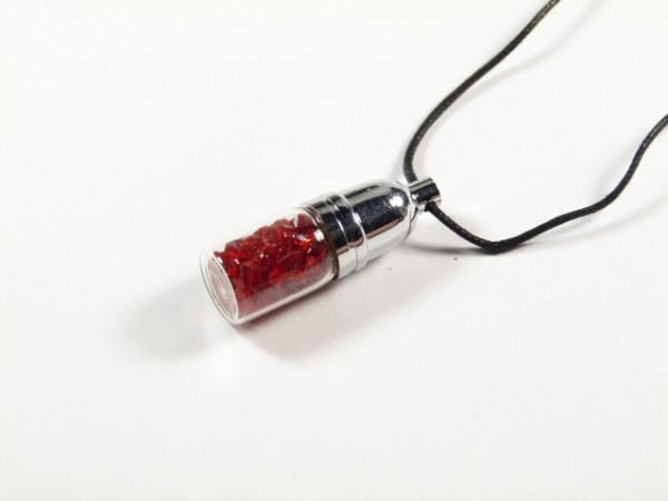 Wisiorek na czarnym sznurku, w kształcie kapsuły, wypełniony czerwonymi kamieniami.