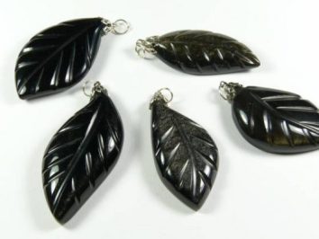 Pięć czarnych wisiorków w kształcie liści leży na białym tle.