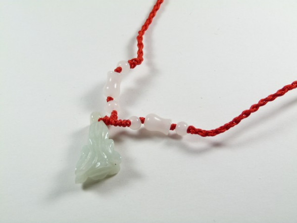 Naszyjnik z czerwonego sznurka z białymi koralikami i zawieszką z jadeitu.