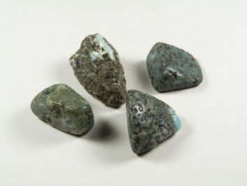 Cztery surowe kamienie larimaru o niebiesko-zielonej barwie na białym tle.