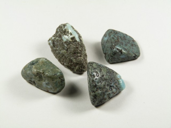 Cztery surowe kamienie larimaru o niebiesko-zielonej barwie na białym tle.