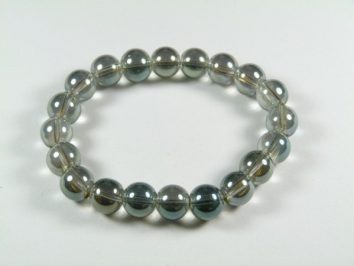 Bransoletka z przezroczystych, szklanych kulek na elastycznej żyłce, leżąca na białym tle.