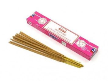 Patyczki zapachowe leżące obok różowego pudełka z napisem „Rose Incense”.