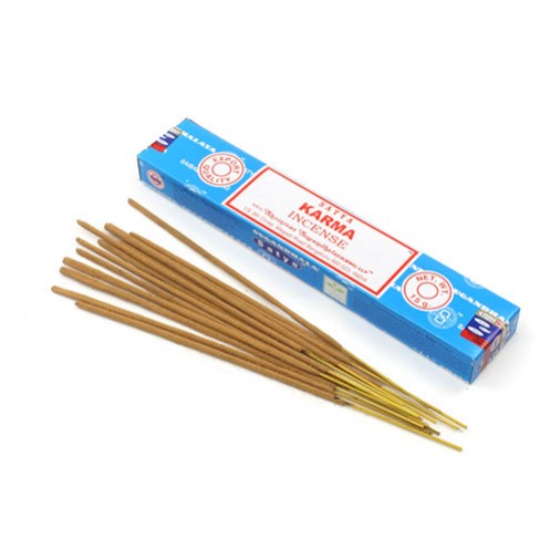 Kilka patyczków kadzidełek leży obok niebieskiego opakowania z napisem "Karma Incense".