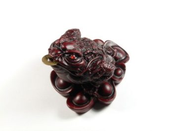 Figurka czerwonej żaby trzymającej monetę w pysku, symbolizująca bogactwo.