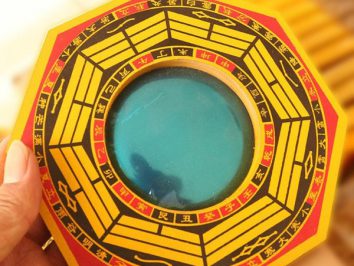 Lusterko bagua wypukłe. Ręka trzyma chińskie lustro bagua z niebieskim szkłem i symbolami feng shui.