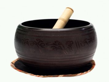 Czarna misa tybetańska z pałeczką leży na podkładce, widoczne są napisy w języku azjatyckim.