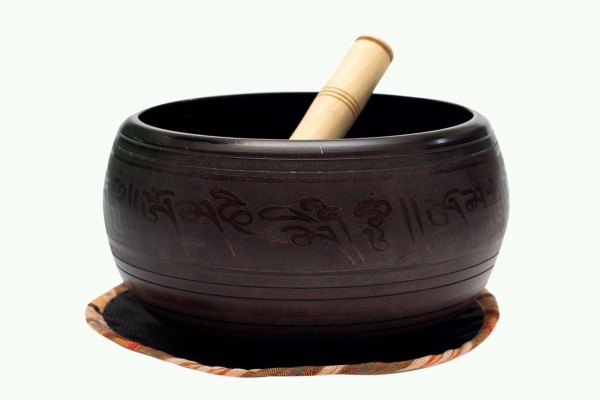 Czarna misa tybetańska z pałeczką leży na podkładce, widoczne są napisy w języku azjatyckim.