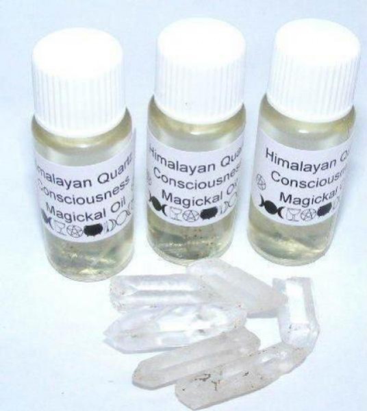 Trzy fiolki z olejkiem i kilka kryształów kwarcu leżące na białym tle.