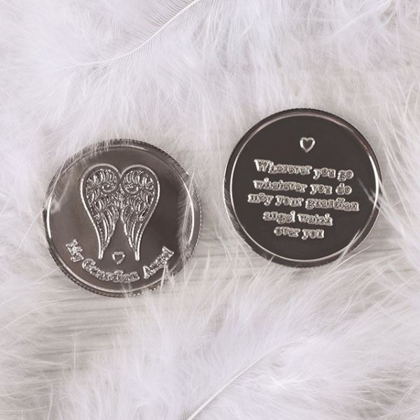 Dwa srebrne medaliki z motywem anielskich skrzydeł, leżące na białych piórkach.