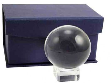 Szklana kula na przezroczystej podstawce przed granatowym pudełkiem.