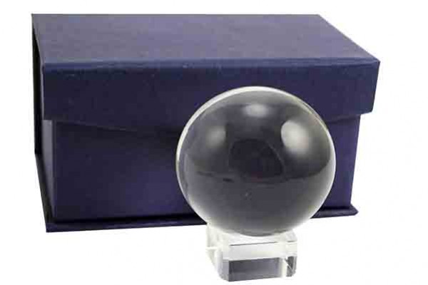 Szklana kula na przezroczystej podstawce przed granatowym pudełkiem.